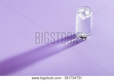 Single Glass With Tonic Water And Ice Cubes On A Purple Background. Coldwater In A Frosty Glass, Hea