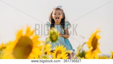 Little Cheerful Girl In A Field Of Yellow Sunflowers. Child And Sunflower, Summer, Nature And Fun. S