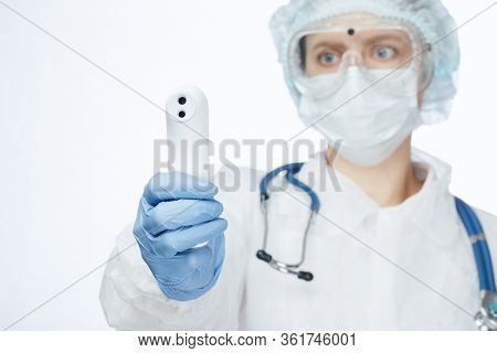 Close-up shot of doctor wearing protective suit abd surgical mask using infrared forehead thermometer (thermometer gun) to check body temperature for virus symptoms - coronavirus outbreak concept
