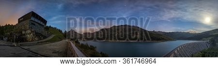 Night Photography Of A Landscape Of The Alps. Lake With Stars In The Sky And Moving Clouds And The M