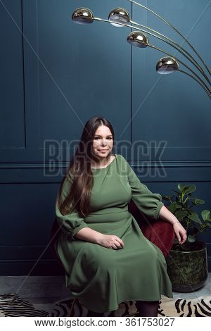 Pretty Young Lady In A Evening Dress Sitting In A Chair On Dark Blue Background. Plus Size Caucasian