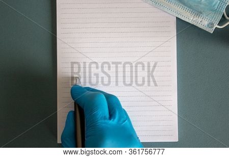 Hand In Blue Glove With Pen And Note On Blue Background. Medicine Mask.
