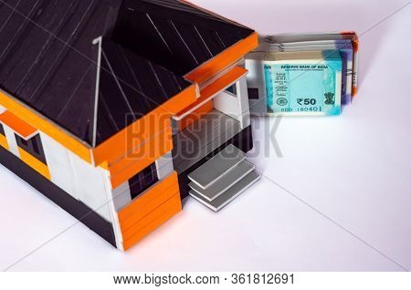 High Angle Shot Of Money Bundles Behind A House Model Made With Craft Materials