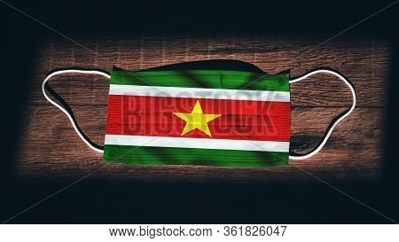 Suriname National Flag At Medical, Surgical, Protection Mask On Black Wooden Background. Coronavirus