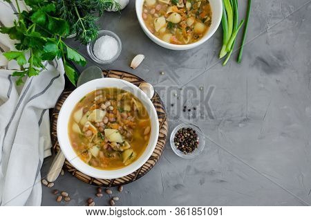 Vegan Soup With Beans And Pasta In A Bowl On A Board On A Dark Concrete Background. Horizontal Orien