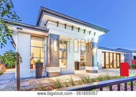 Luxury House Facade Over The Metal Fence Under Blue Sky, There Are Trees And Gravel On The Ground Of
