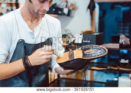 Shoemaker putting glue on sole of a shoe to fix