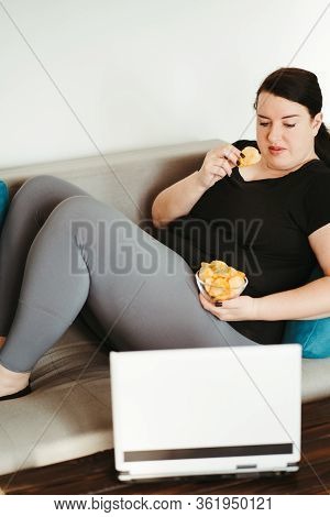 Overeating And Gluttony Concept. Mindless Snacking, Home Sedentary Lifestyle. Obese Woman Sitting On