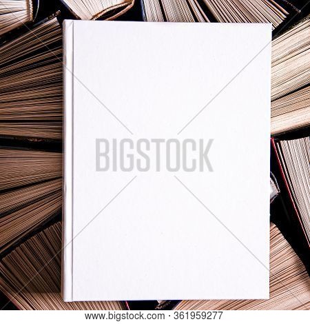 Mockup Of Closed Blank Square Book Rests On Open Old Multicolored Books