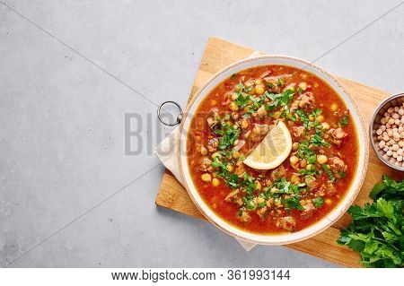 Moroccan Harira Soup In White Plate On Woden Board On Grey Concrete Table Top. Harira Is Moroccan Cu