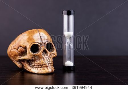 Skull Of A Dead Man With An Hourglass On A Dark Background. Concept, Symbol Of The Transience Of Lif