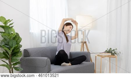 Beautiful Asian woman stretches out her arms on her favorite sofa in the living room, Body and mind 