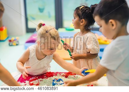Fun Sensory Play With Moldable Kinetic Sand At Nursery School. Toddlers Standing Around The Table An