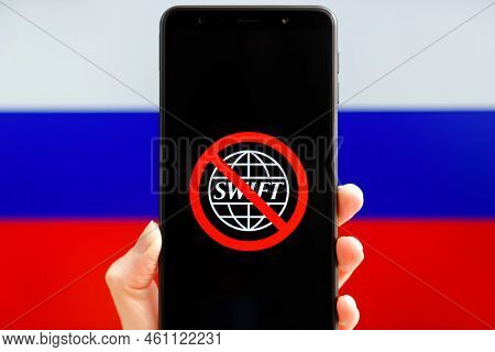 Ukraine, Kiev - February, 23 2022: Hand Holding Mobile With Crossed Out Swift Logo And Russian Flag 