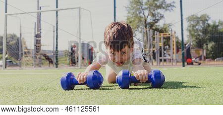 A Child With Dumbbells On The Playground. A Sporty Kid. Illustrating An Article About Sports. Childr