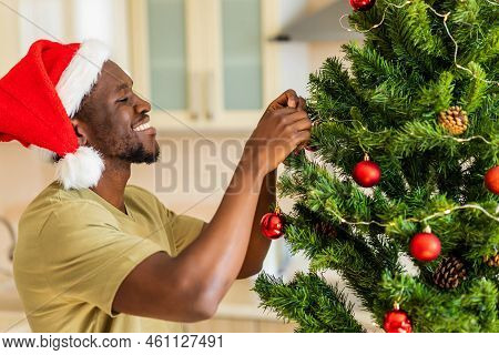Afro American Man In Santa Hft Decorate The Christmas Tree With A Red Ball At Home