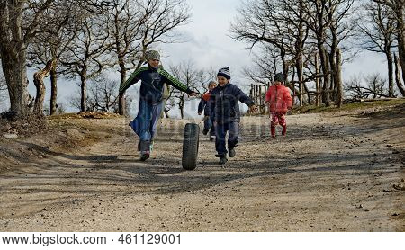 Dubki. Russia. April 03, 2021. A Group Of Children Of Different Ages Run After A Big Wheel. Which Ro