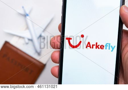 Arkefly Airline Application On The Smartphone Screen Mans Hand. A White Toy Airplane And A Passport 