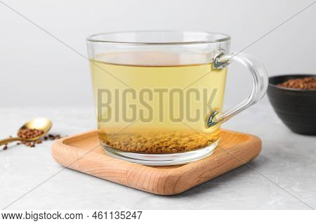 Cup Of Aromatic Buckwheat Tea And Granules On Light Marble Table, Closeup