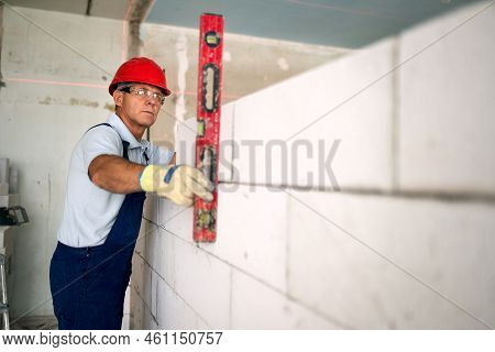 Bricklayer Using Spirit Bubble And Laser Level To Precise Check Concrete Blocks On Wall. Contractor 