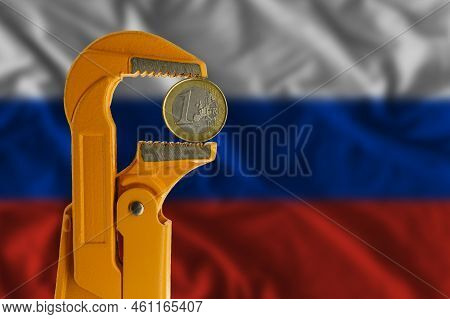 One Euro Coin Held In An Orange Plumber Wrench On The Background Of The Russian Flag. Reverse Side