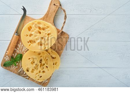 Cheese Maasdam Or Radamer. Piece Of Cheese On Wooden Stand Board On White Wooden Table Background. T