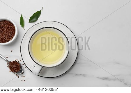 Cup Of Buckwheat Tea And Granules On White Marble Table, Flat Lay. Space For Text