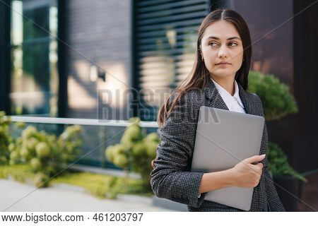 Young Caucasian Businesswoman With Confident Look, Holding A Laptop In Her Hands Standing Outside Of