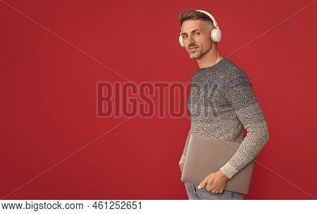 Happy Guy In Casual Listen To Audio Course In Headphones Holding Laptop Red Background, E-school