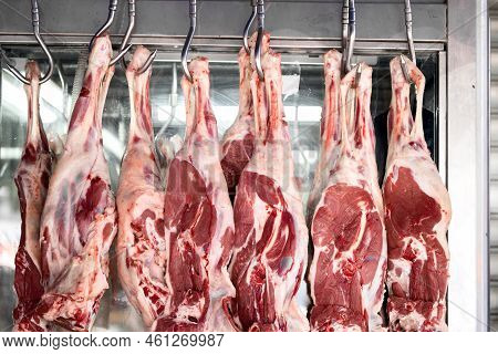 Raw Mutton Or Lamb Legs Hanging On Butcher Hooks