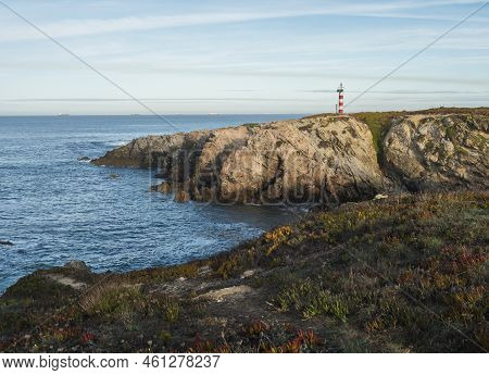 View Of The Sea And Cliffs With The Red And White Lighthouse At Praia Pequena Beach At Wild Vicentin