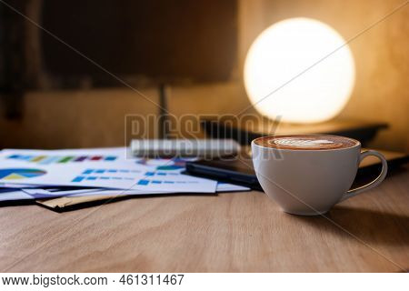 Closeup View, White Cup Of Coffee With Tablet Computer, Notebook And Chart Of Investment On Table In