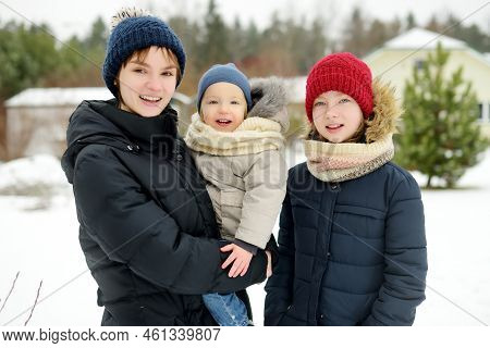 Two Big Sisters And Their Toddler Brother Having Fun Outdoors. Two Young Girls Holding Their Sibling