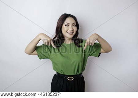 Excited Asian Woman Wearing Green T-shirt Pointing At The Copy Space Downside Her, Isolated By White