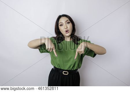 Shocked Asian Woman Wearing Green T-shirt Pointing At The Copy Space Downside Her, Isolated By White