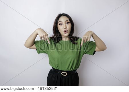 Shocked Asian Woman Wearing Green T-shirt Pointing At The Copy Space Downside Her, Isolated By White
