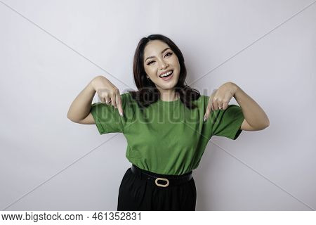 Excited Asian Woman Wearing Green T-shirt Pointing At The Copy Space Downside Her, Isolated By White