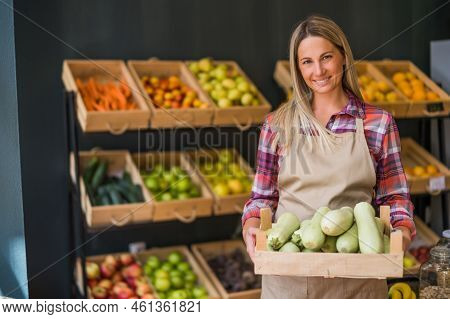 Woman Works In Fruits And Vegetables Shop. She Is Holding Basket With Marrow Squash.