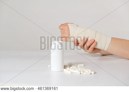 A Persons Hand With An Elastic Bandage And A Jar Of Calcium Or Chondroitin Tablets. Treatment Of Fra