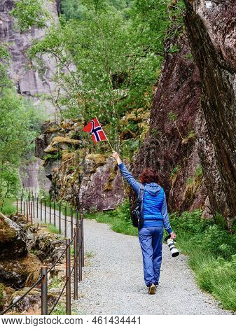 Tourist Woman With Norwegian Flag And Camera Walking Trough Mountains Path In Allmannajuvet Area Sau