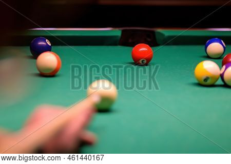 Billiard Balls In A Green Billiard Table. Blurred Hand With Cue Pointing At Billiard Ball At Table