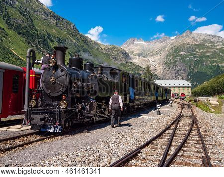 Gletsch, Switzerland - July 15, 2022: A Historic Train With A Steam Locomotive On The Furka Railway 