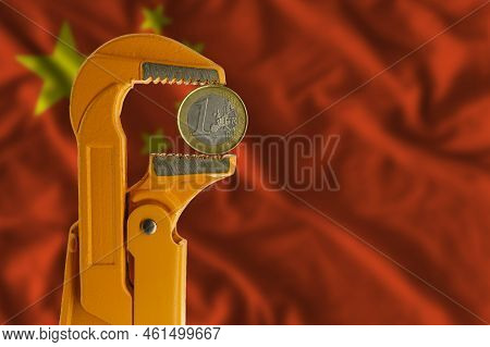 One Euro Coin Clamped In An Orange Plumber Wrench On The Background Of The Flag Of China. Reverse Si