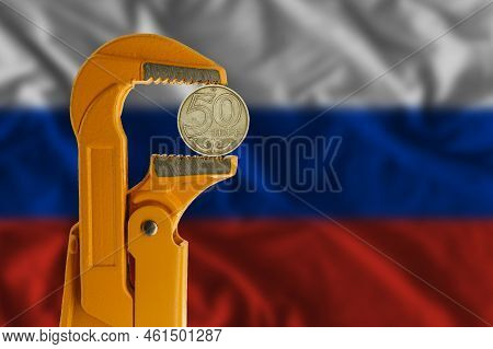 50 Kazakhstani Tenge Coin Clamped In An Orange Plumber Wrench On The Background Of The Russian Flag.