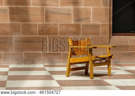Sling Chair. Empty Modern Leather And Wood Lounge Seat Alone In Empty Space With Tiled Floor And Wal