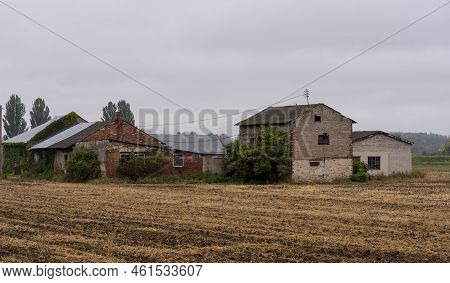 Old Farm Buildings Made Of Stone And Bricks With Roofs Covered With Sheet Metal, Tiles, And Eternit 