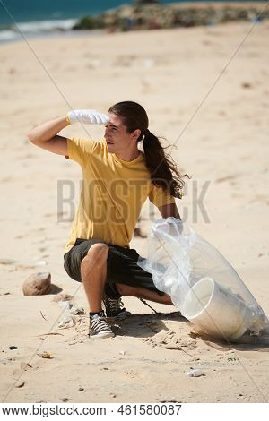Young Man Wearing Gloves When Collecting Garbage On Beach In Plastic Bag
