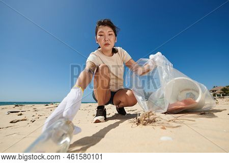 Serious Female Volunteer Collecting Garbage On Sandy Beach