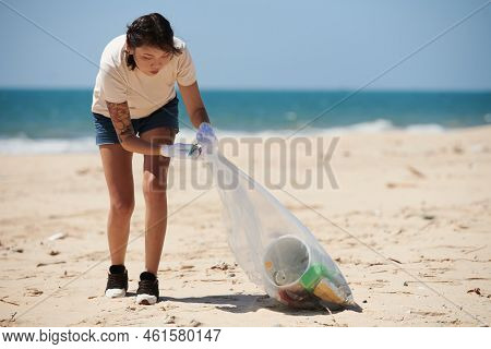 Young Woman Cleaning Up Sea Beach, Collecting Trash Into Plastic Bag