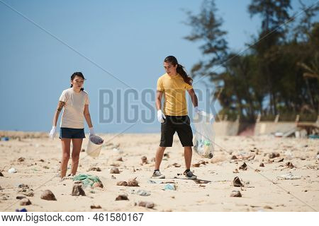 Young Couple Collecting Debris And Garbage Left By Tourists On Sea Beach